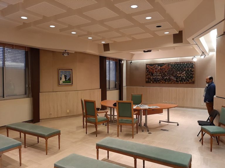 Salle de réunion avec plafond acoustique en caissons, enceintes murales et table ovale entourée de chaises