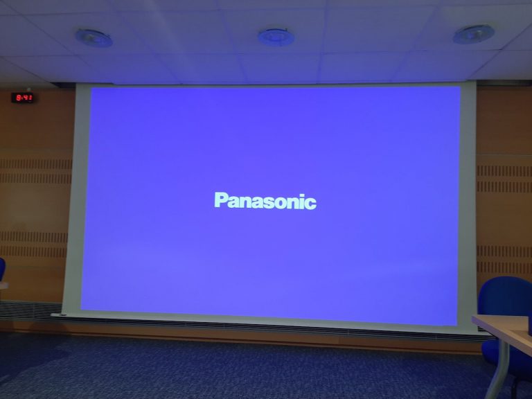 Écran de projection motorisé affichant le logo Panasonic dans une salle aux panneaux acoustiques en bois