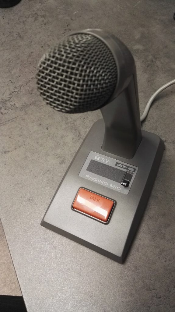 Microphone d'appel de bureau TOA avec bouton d'annonce, posé sur un comptoir