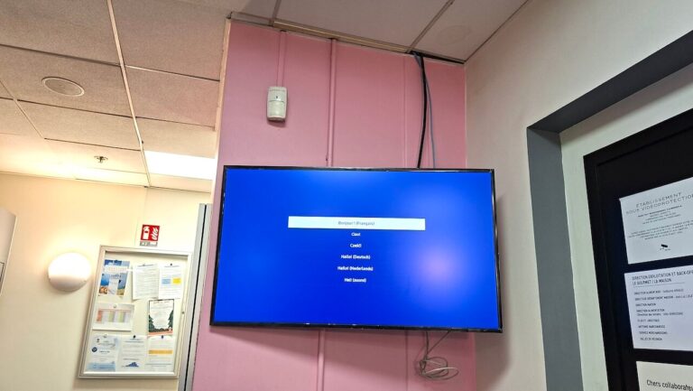 Écran mural affichant l'assistant de configuration Samsung, fixé sur un mur rose dans un couloir de service