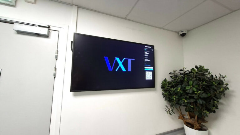 Écran mural affichant l'interface de connexion VXT avec QR code d'appairage, dans un espace de bureaux